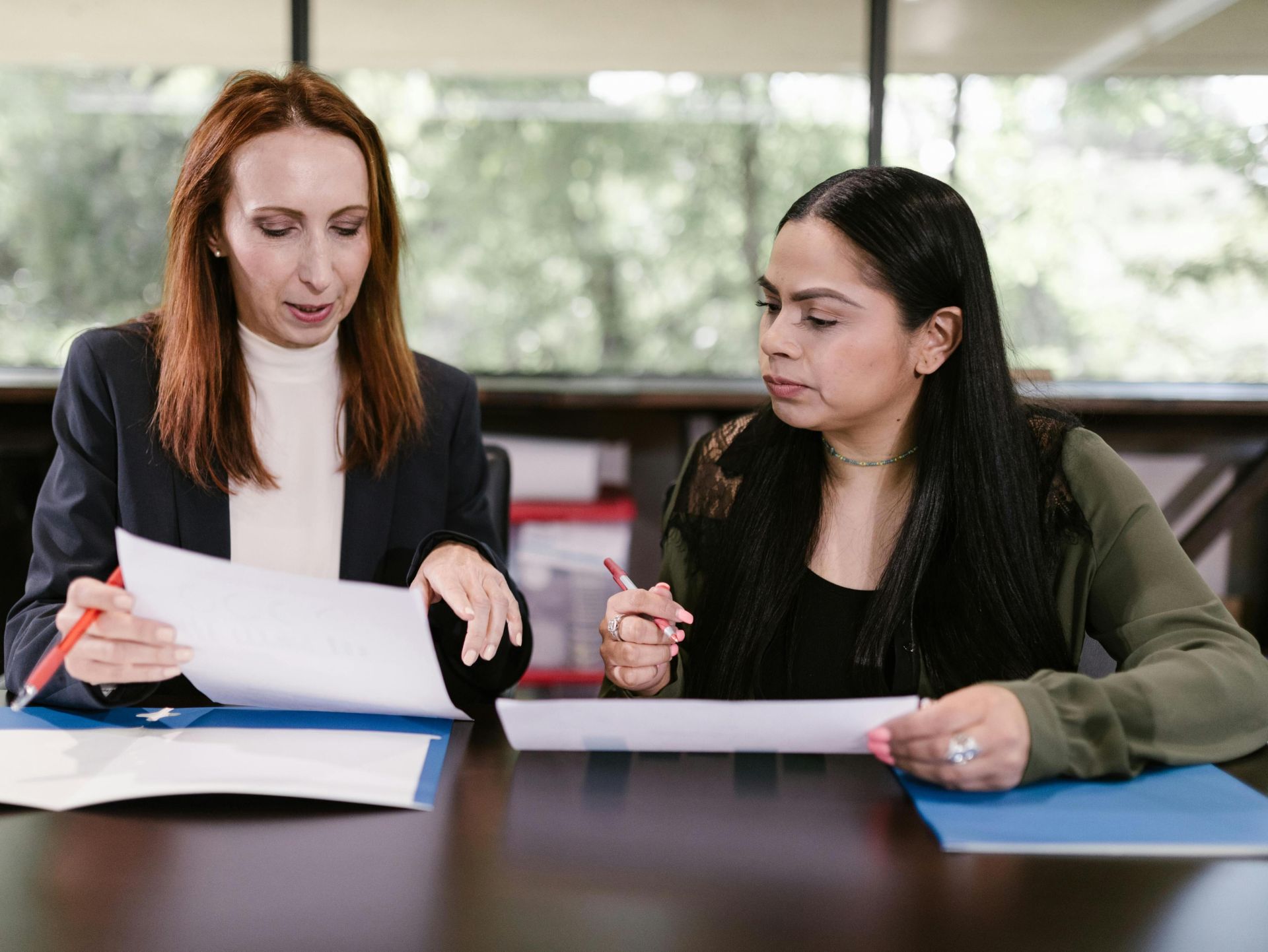 Two professional women reviewing documents in a well-lit office setting.